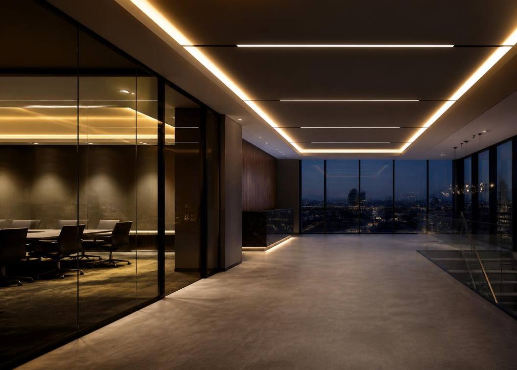 Contemporary office interior at dusk lit by recessed linear ceiling lighting and illuminated coves.